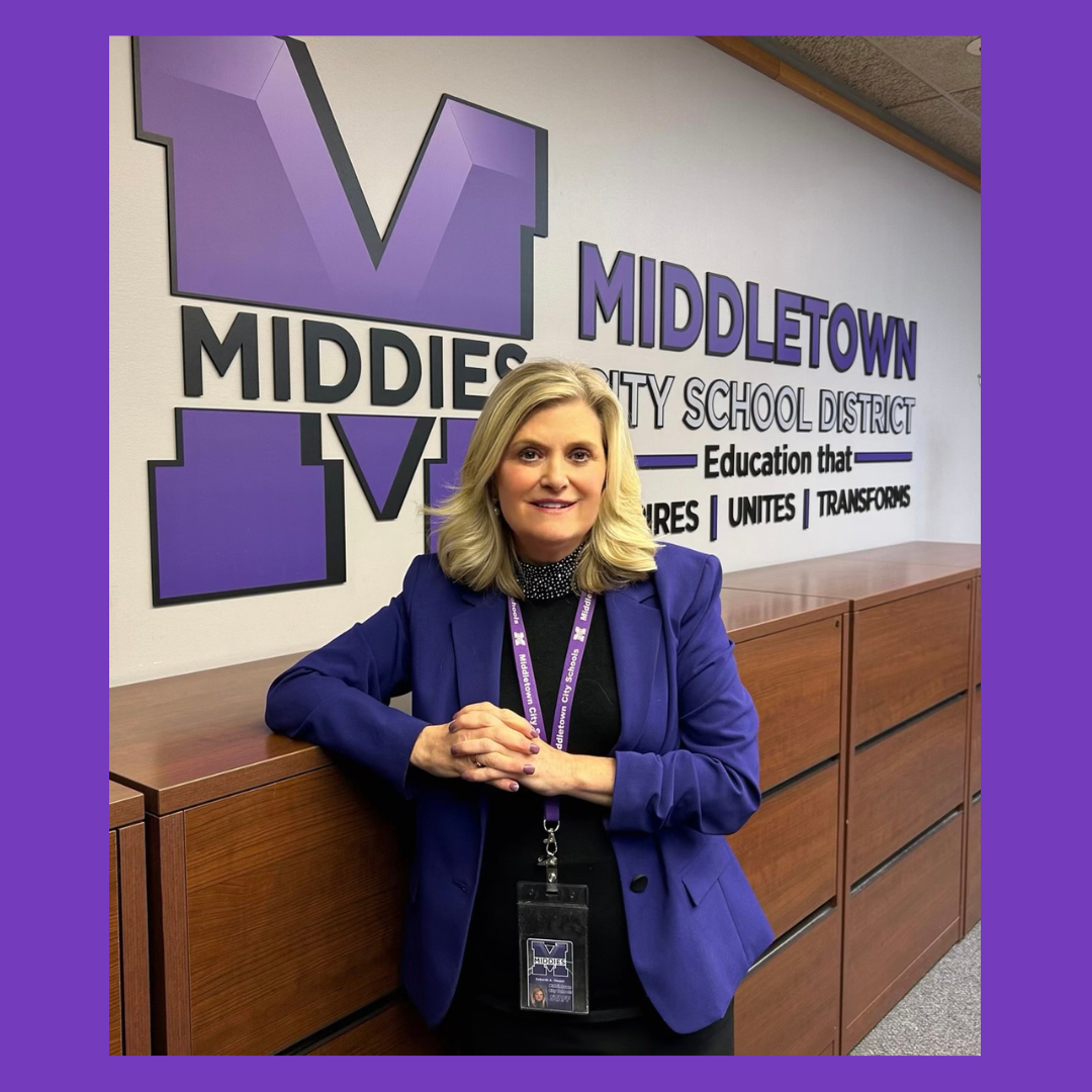 Blonde woman wearing purple blazer with MCSD sign behind her